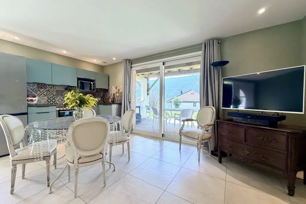 vue de la salle à manger cuisine avec 1 table 5 chaises une télévision et cuisine équipé avec accès terrasse