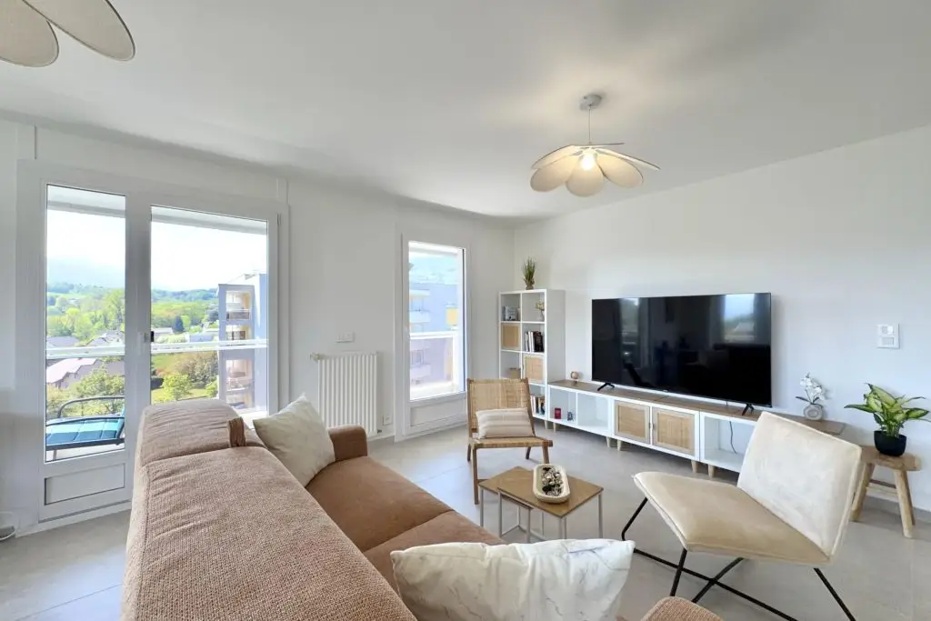 salon avec canapé, table basse, 2 fauteuils, grande télévision, meuble de rangements et 2 accès balcon