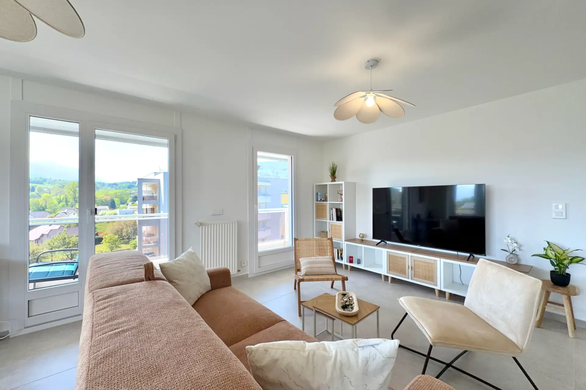 salon avec canapé, table basse, 2 fauteuils, grande télévision, meuble de rangements et 2 accès balcon